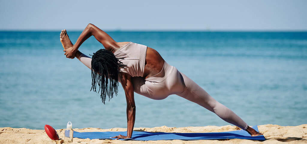 Woman doing a difficult yoga pose on a sunny beach